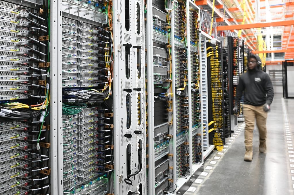 Rows of network racks with high-density patch panels and colour-coded cabling, with an engineer walking the aisle