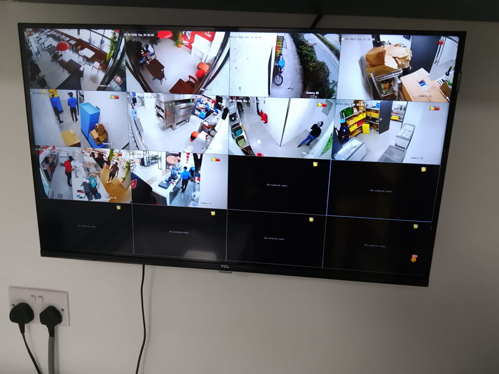 A wall-mounted monitoring screen showing a live multi-camera view of the dining area, kitchen, store room, entrance and service counter.